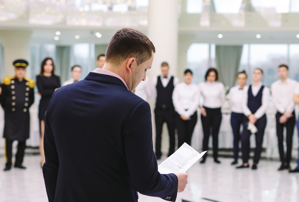 Elite Hotel Services - Mann im Anzug, mit einem Blatt Papier in der Hand, steht vor aufgereihtem Hotelpersonal